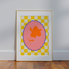 The Framed Magnolia Capri Wall Art by Good Juju Homeware features vibrant orange and pink florals on a yellow-white checkered background. Leaning against a light gray wall on a wooden floor, it adds unique style to any space.