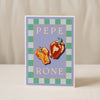 The Pesto Greeting Card by Good Juju Homeware showcases two illustrated bell peppers and "PEPE RONE" on a blue and green checkered border, bringing Mediterranean charm to any occasion.