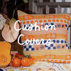 Colorful cushion with orange and blue pattern, placed behind a bouquet with anthurium flowers, a squash, and tomatoes. Text says "Cushion Covers.