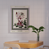 A minimalist room features a wooden table, two chairs with purple seats, and a plant. The "Poppies in a Glass Vase Venice Wall Art" from Good Juju Homeware adds funky sophisticated florals to the space, completing it with vibrant elegance.