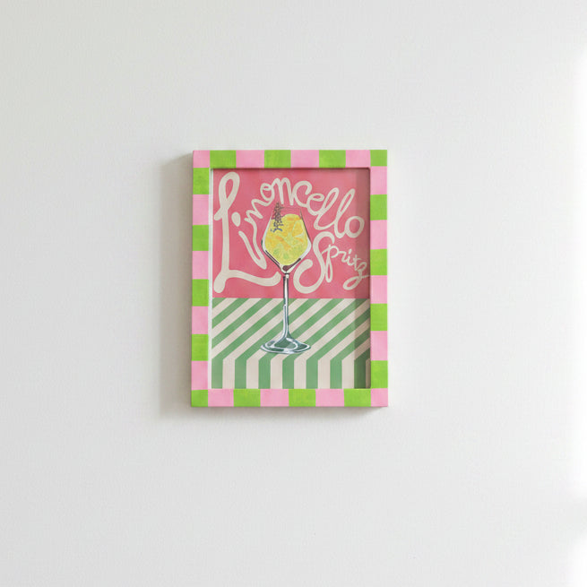 The A5 Navy and Light Blue Painted Frame from Good Juju Homeware displays a striped cocktail art print with “Limoncello Spritz” text, creating unique wall decor against a white wall.