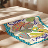 Colorful towel with decorative eggs and 'Cotter & Longwell' branding on a wooden surface.