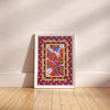 A framed art print featuring a colorful pattern of red tomatoes, blue bowls, and yellow decorative borders on a burgundy background, leaning against a beige wall on a light wood floor.