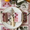 A charming table setting features elegant tableware: a white plate, fork, knife, glassware, and the Poppy Stripe Venice Napkin. Lemons add zest to the Calla Lily Check patterned tablecloth from Good Juju Homeware.