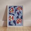 The "Poppies All Around Milan" wall art from Good Juju Homeware features a framed abstract print with red, white, and blue floral shapes. Lean it against a wall on a wooden floor for the perfect addition to your collection.