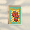 The Zuchini Greeting Card by Good Juju Homeware features an illustrated zucchini vine and "ZUCCHINI" in bold letters on a yellow and green striped background, adding Mediterranean charm to premium card stock.